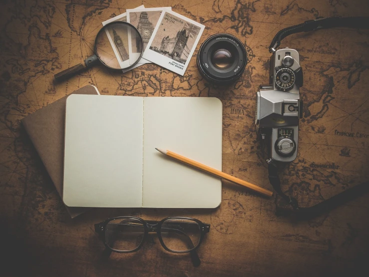 an open notebook sitting on top of a table next to a camera, a picture, visual art, with navigator shaped glasses, vintage vibe, knolling, sepia colors