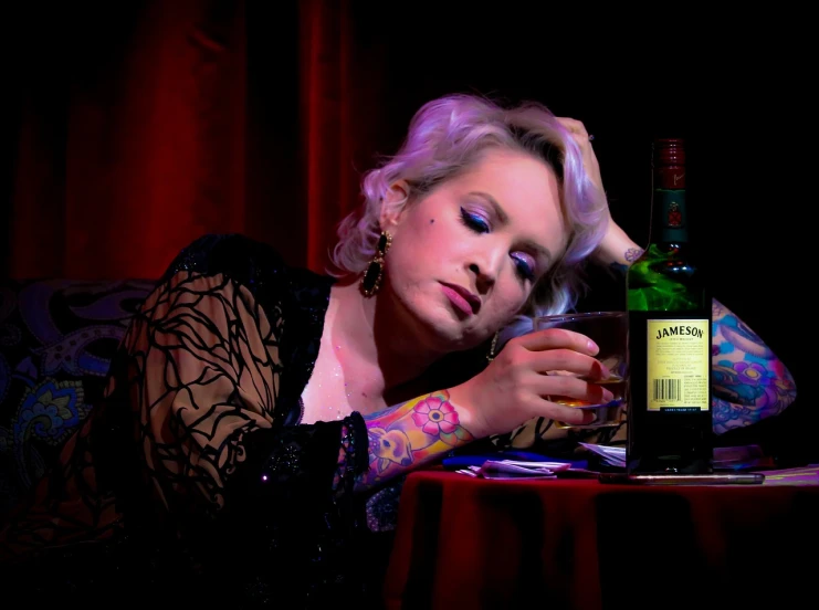 a woman sitting at a table with a bottle of wine, a portrait, by James Warhola, pexels, romanticism, burlesque psychobilly, elisabeth moss, stage photography, & her expression is solemn