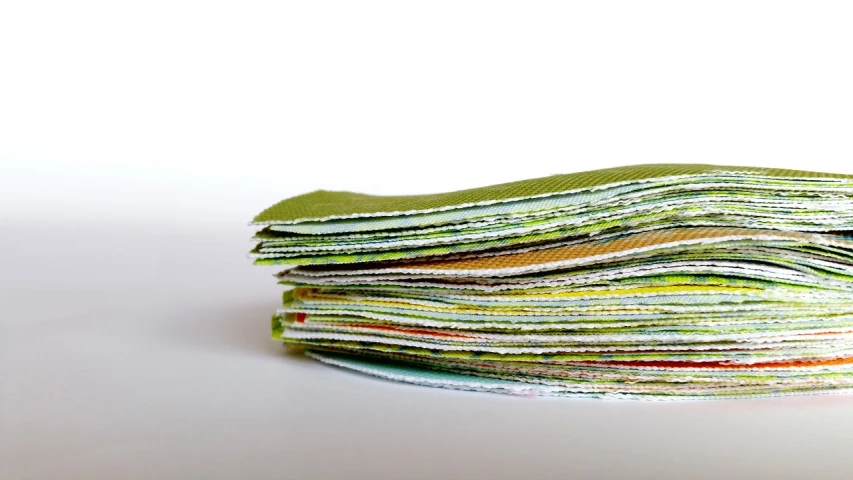 a stack of folded papers sitting on top of a table, by Anita Kunz, process art, seams stitched tightly, green and yellow tones, profile close-up view, towels