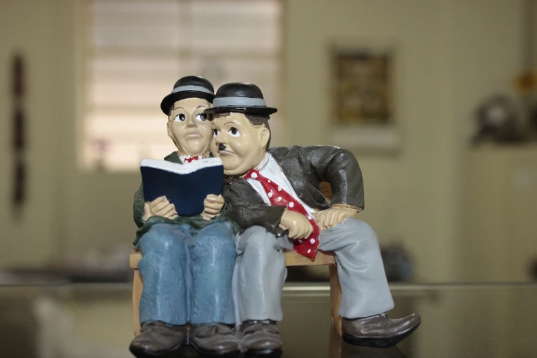 a couple of figurines sitting on top of a table, inspired by Norman Rockwell, flickr, figuration libre, nathan fielder and groucho marx, woody\'s homework, with one vintage book on a table, sitting in a waiting room