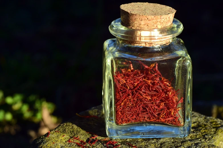 a jar of saffron sitting on a rock, a macro photograph, pixabay, art nouveau, bottles of spices, with backlight, on a sunny day, red velvet