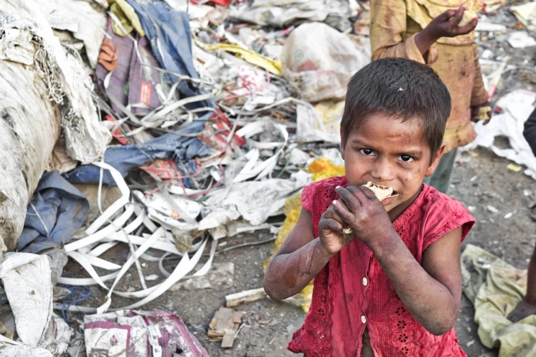 a small child standing in front of a pile of garbage, eating, hindu, year 3022, handsome girl