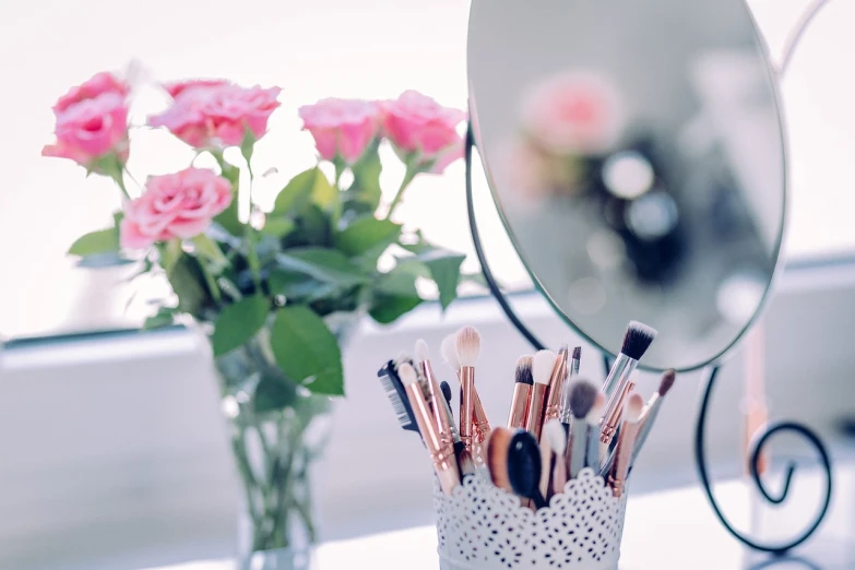 a vase filled with makeup brushes next to a mirror, by Maksimilijan Vanka, pexels, romanticism, roses, bright daylight indoor photo, half image, with soft bushes