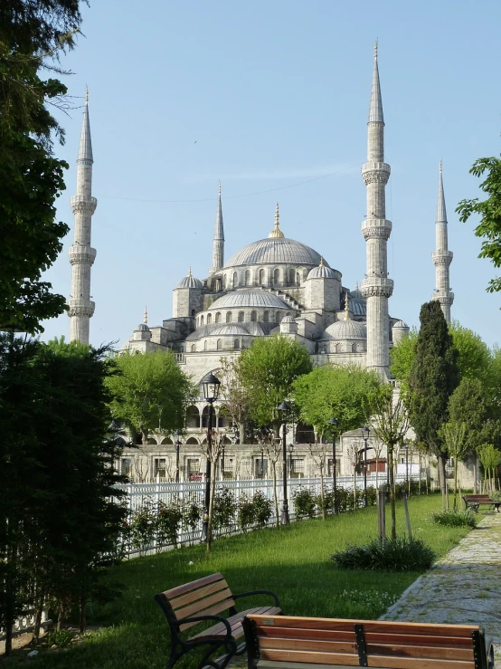 a bench sitting in front of a large building, inspired by Altoon Sultan, flickr, hurufiyya, black domes and spires, lush surroundings, blue, grayish