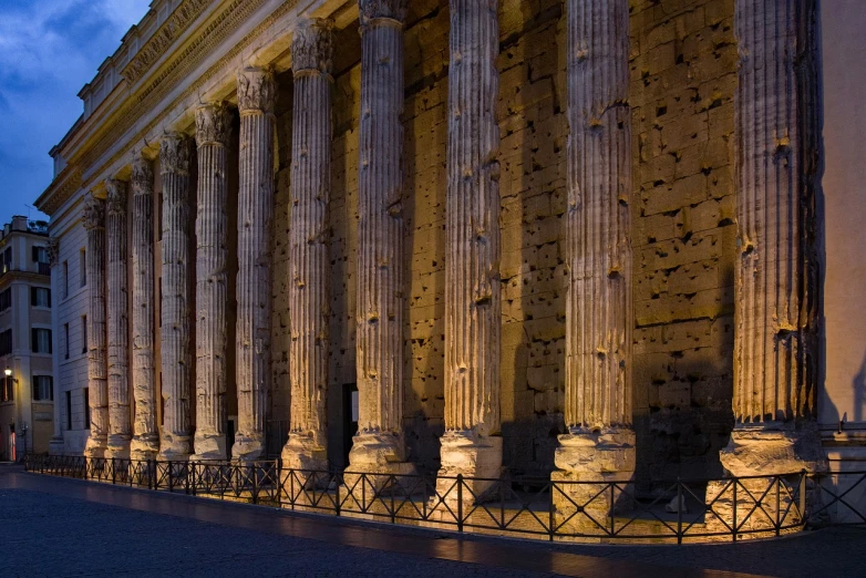 the columns of a building are lit up at night, by Robert Griffier, shutterstock, ancient roman setting, high resolution and detail, hard morning light, set photo