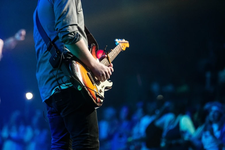 a man playing a guitar in front of a crowd, pexels, details and vivid colors, accentuated hips, concert photo, in profile