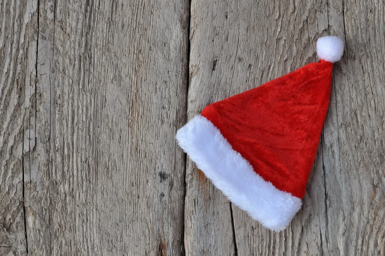 a santa hat sitting on top of a wooden table, a photo, pexels, folk art, background image, seams, profile image, wallpaper - 1 0 2 4