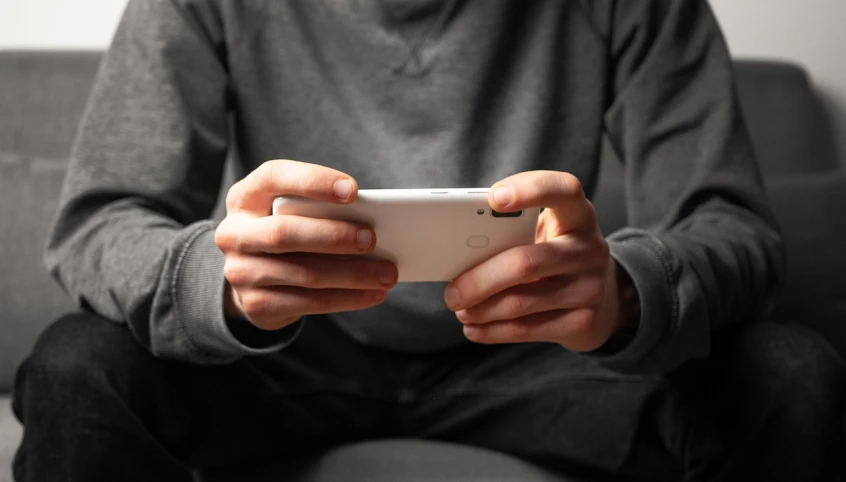 a person sitting on a couch holding a cell phone, a picture, gaming, hands retouched, male teenager, grayish