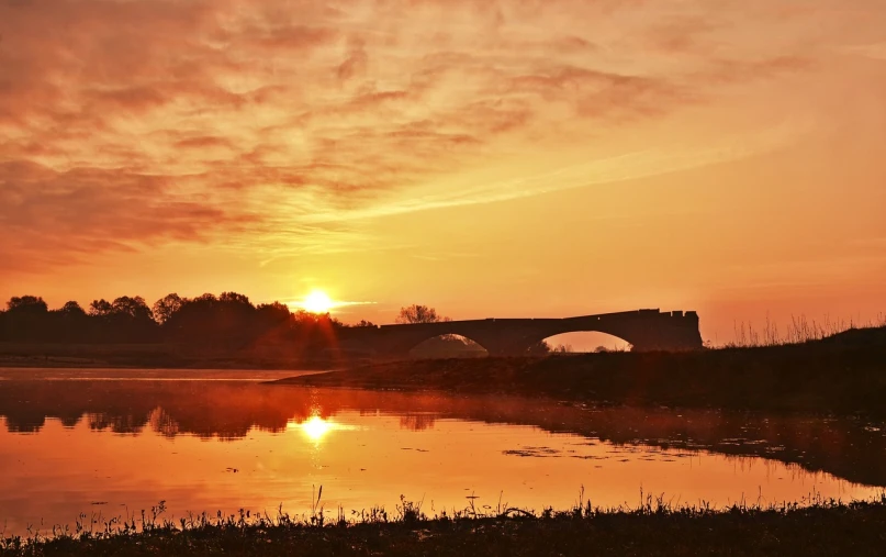 a sunset over a body of water with a bridge in the background, a picture, by Istvan Banyai, flickr, romanticism, at sunrise in springtime, red river, stone bridge, mid shot photo