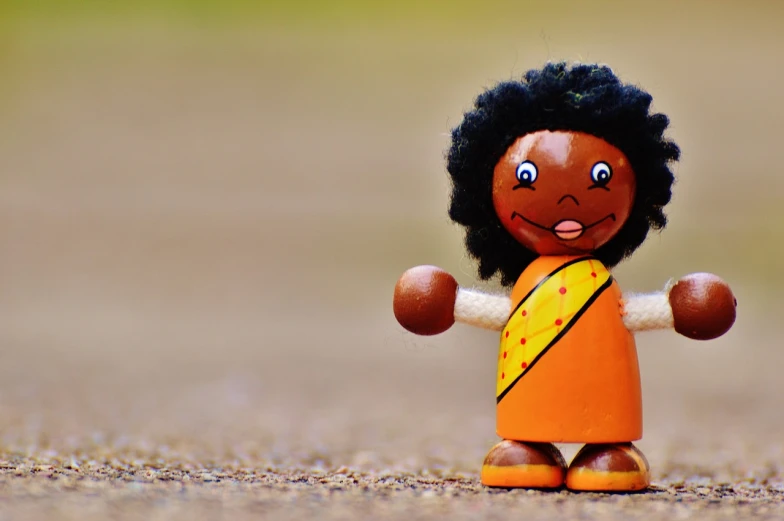 a close up of a toy doll on the ground, pexels contest winner, african woman, welcoming attitude, cute funny figurine wooden, orange body