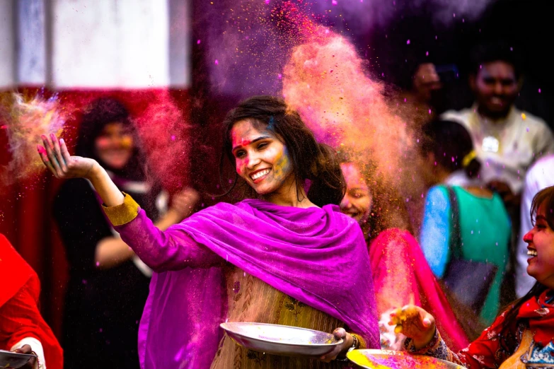 a woman is throwing colored powder on her face, dressed in a sari, 🤬 🤮 💕 🎀, smiling and dancing, colorful crowd