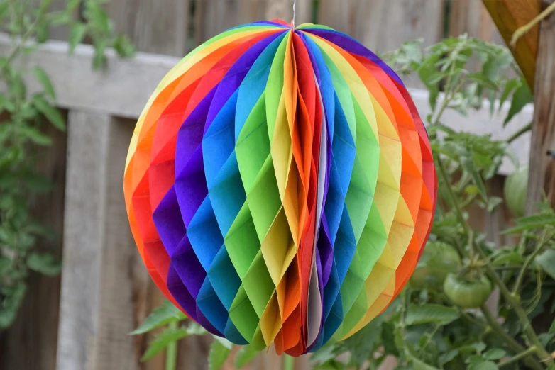 a colorful paper ball hanging from a tree, honeycomb halls, rainbow diffraction, 2 1 0 mm, tonal colors outdoor