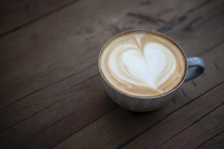 a cup of coffee sitting on top of a wooden table, by Adam Chmielowski, hearts, round-cropped, brown and white color scheme, photograph credit: ap