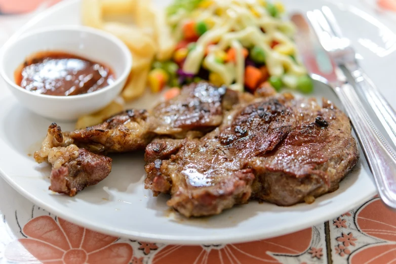 a white plate topped with meat next to a bowl of sauce, shutterstock, manila, mutton chops, 🕹️ 😎 🔫 🤖 🚬, gintas galvanauskas