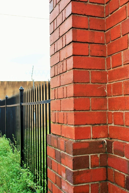 a fire hydrant sitting on the side of a brick building, shutterstock, fence, iron cladding, looking around a corner, pillar