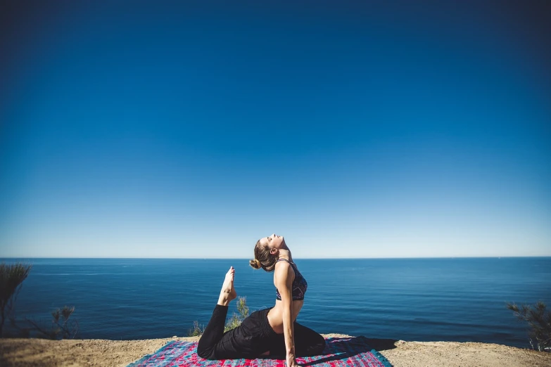 a woman doing a yoga pose in front of the ocean, a picture, on a bright day, usa-sep 20, iconic shot, view from the top