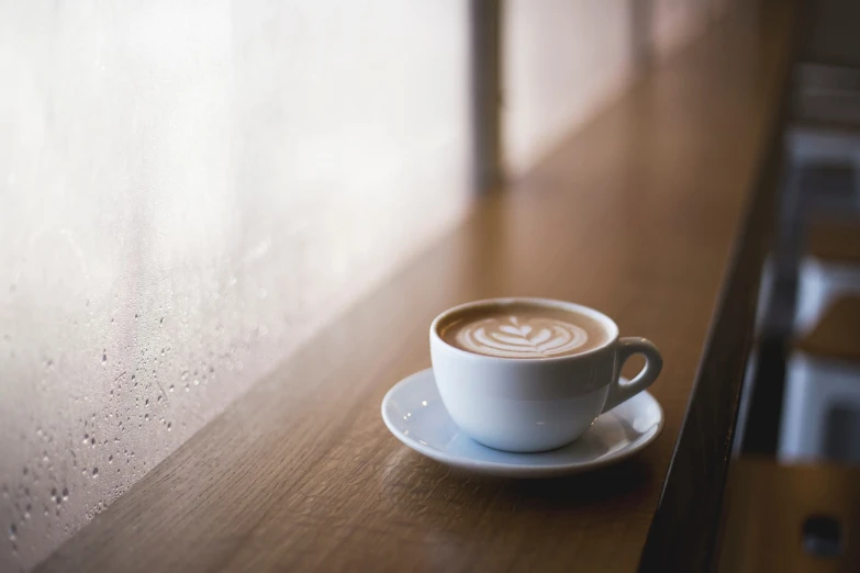 a cup of coffee sitting on top of a wooden table, a picture, shutterstock, soft window light, sitting in a cafe alone, high detail shot, latte art