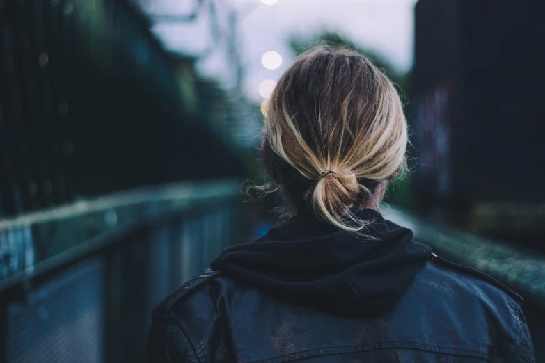 a woman in a black jacket standing on a bridge, unsplash, back of the hair, a round minimalist behind, on the streets, his back is turned