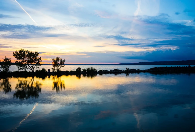a body of water with a sunset in the background, a picture, by Karl Hagedorn, shutterstock, at sunrise in springtime, wide wide shot, blue reflections, bay