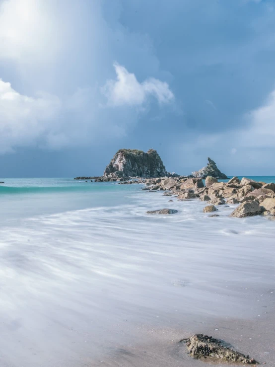 a white surfboard sitting on top of a sandy beach, a tilt shift photo, by Alexander Robertson, unsplash contest winner, epic matte painting of an island, wellington, long exposure photo, the rock is in the sea