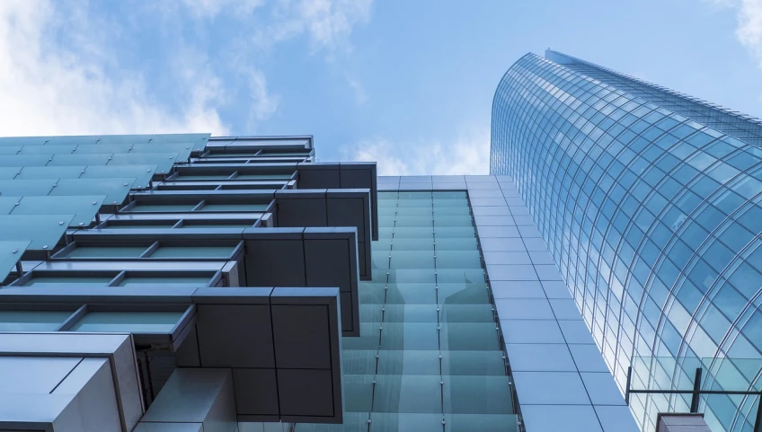 a couple of tall buildings next to each other, inspired by Richard Wilson, unsplash, lots of glass details, blue and clear sky, commercial banner, low - angle shot from behind