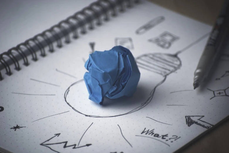 a piece of paper sitting on top of a notebook, concept art, by Aleksander Gierymski, conceptual art, lightbulb, rendering a blue rose, design thinking, abstract claymation