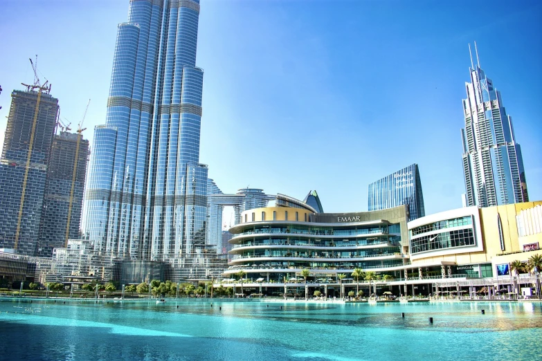 a large body of water surrounded by tall buildings, hurufiyya, epic buildings in the center, full of clear glass facades, oasis in the desert, beautiful day