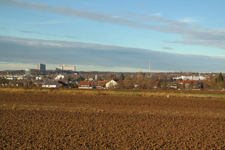 a plowed field with buildings in the background, a picture, flickr, bauhaus, late autumn, entire city in view, hardturm, slightly sunny