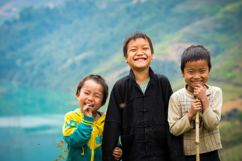 a group of three children standing next to each other, by John La Gatta, shutterstock, vietnam, near a lake, in the hillside, big smile