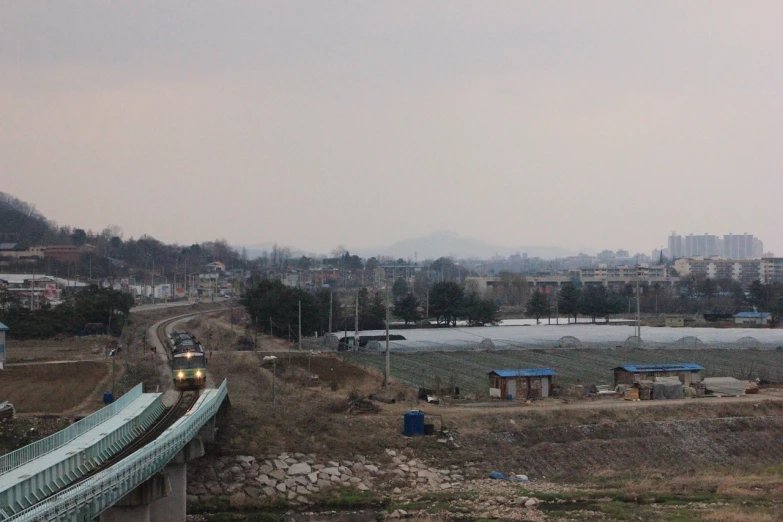 a train traveling over a bridge over a river, inspired by Choi Buk, flickr, korean countryside, urban view in the distance, pentagon, late morning