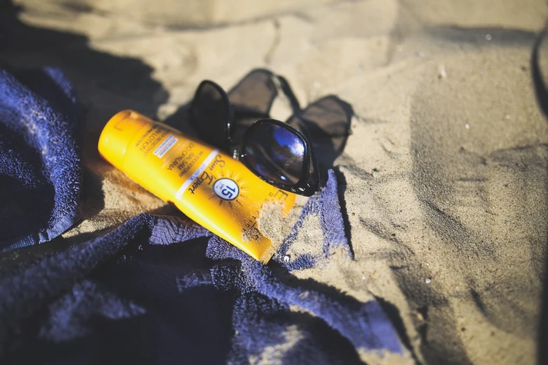 a bottle of sunscreen sitting on top of a towel, a picture, by Thomas Häfner, pexels, golden glow, 🕹️ 😎 🔫 🤖 🚬, shades, beach on the outer rim