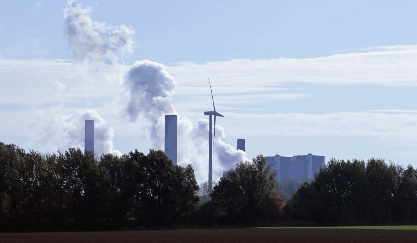 a wind turbine in a field with a factory in the background, a picture, by Werner Gutzeit, pexels contest winner, purism, puffs of thick black smoke, wikimedia commons, view from a distance, 15081959 21121991 01012000 4k