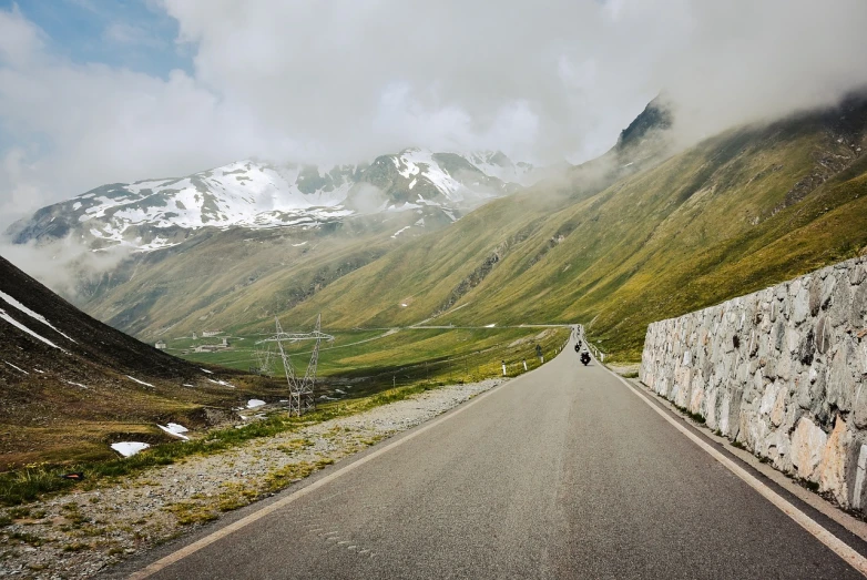 a man riding a bike down the middle of a road, by Werner Andermatt, gigantic landscape!, snow capped mountains, with fog, julia hetta