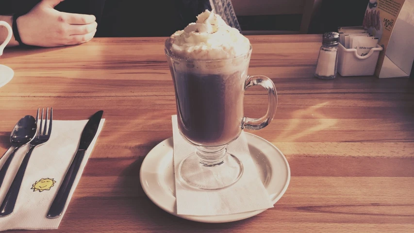 a person sitting at a table with a cup of coffee, whipped cream, hurricane, in a pub, photo taken with an iphone