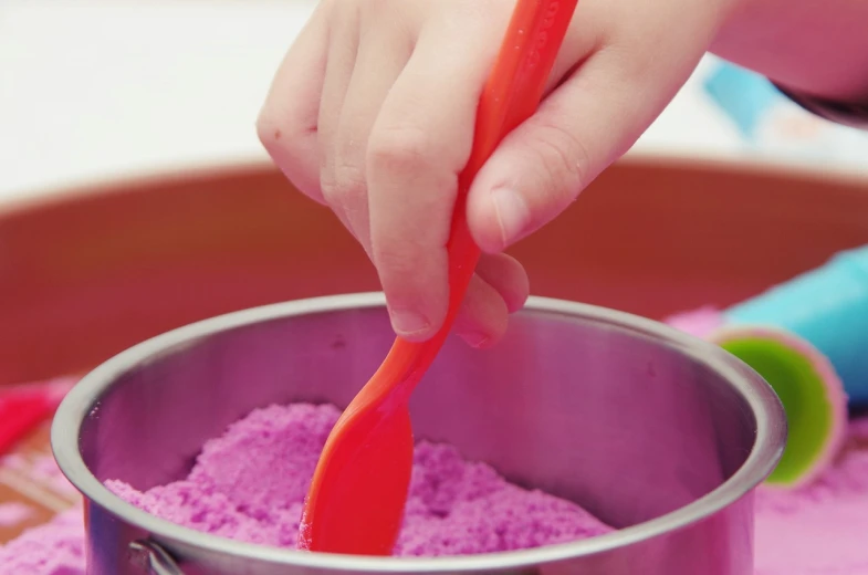 a close up of a child's hand with a red spoon, a pastel, purple sand, vertical orientation, product introduction photo, pot