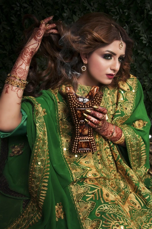 a woman in a green dress holding a cell phone, a portrait, inspired by Osman Hamdi Bey, shutterstock, arabesque, mehndi patterns, fashion portrait photo, high quality fantasy stock photo, encrusted with jewels