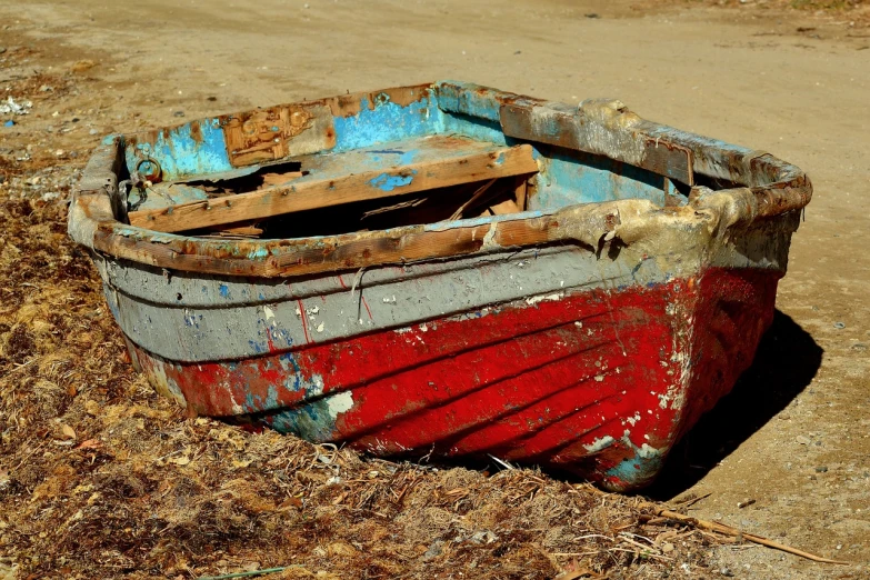 a red and blue boat sitting on top of a dirt field, a photo, by Richard Carline, pixabay, renaissance, weathered olive skin, photorealism. trending on flickr, skiff, cracked varnish
