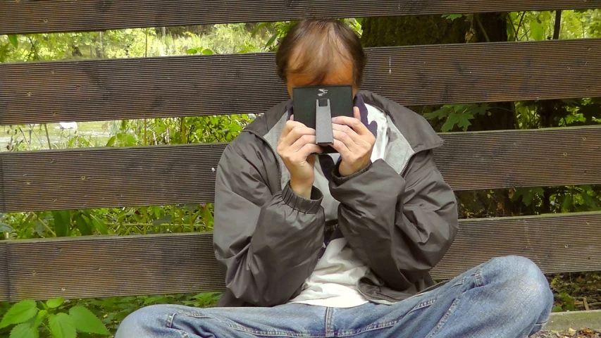 a person sitting on a bench holding a cell phone, a picture, by Jan Rustem, flickr, chewing on a video card, hood covers his eyes, [ realistic photo ]!!, stable diffusion self portrait