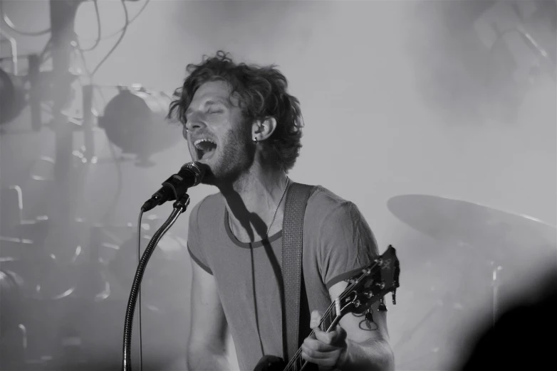 a man singing into a microphone while holding a guitar, a picture, inspired by James Morrison, under a gray foggy sky, phosphorescent, bedhead, ((oversaturated))