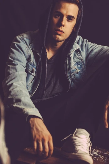 a man sitting on top of a wooden table, a picture, pexels, realism, wearing jeans and a black hoodie, portrait of depressed teen, jean jacket, sensual and beautiful incubus