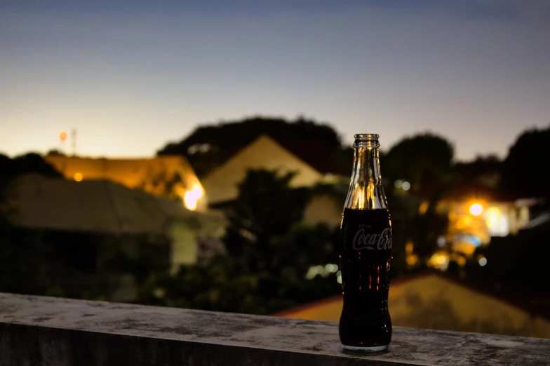 a bottle of coke sitting on top of a cement ledge, a picture, by Alexander Fedosav, pexels contest winner, window to night time, farol da barra, today\'s featured photograph 4k, sweet night ambient