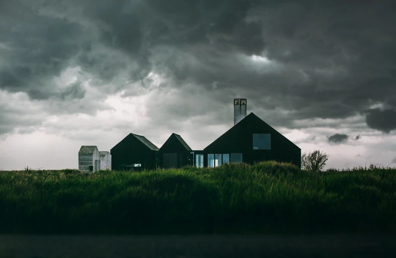 a couple of houses sitting on top of a lush green hillside, by Jesper Knudsen, unsplash contest winner, modernism, ominous nighttime storm, beautiful dark beach landscape, black steel buildings, front view dramatic