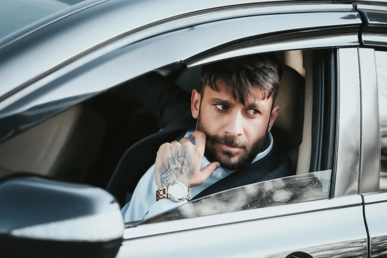a man sitting in the passenger seat of a car, a photo, shutterstock, very attractive man with beard, luxury lifestyle, with facial tattoo, stock photo