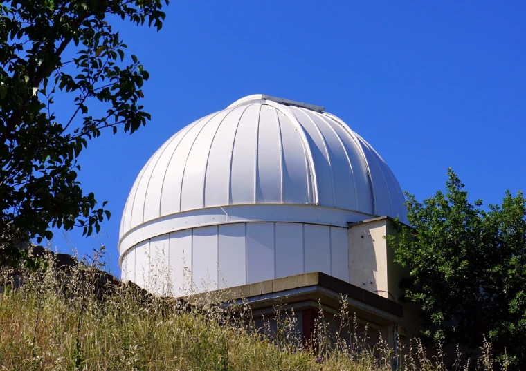 a white dome sitting on top of a lush green hillside, a photo, by John Covert, shutterstock, telescope, front top side view, seattle, rounded roof