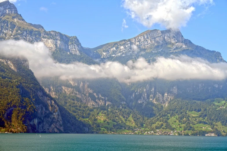 a large body of water with mountains in the background, a picture, by Sigmund Freudenberger, shutterstock, lauterbrunnen valley, covered in clouds, harbor, steep cliffs