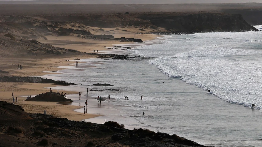 a group of people standing on top of a beach next to the ocean, by Peter Churcher, afp, desert, people swimming, slight overcast weather