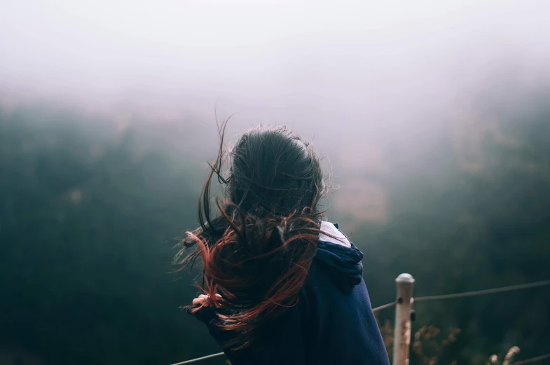 a woman with her hair blowing in the wind, pexels contest winner, realism, foggy jungle in the background, looking out into space, tiny girl looking on, hair down