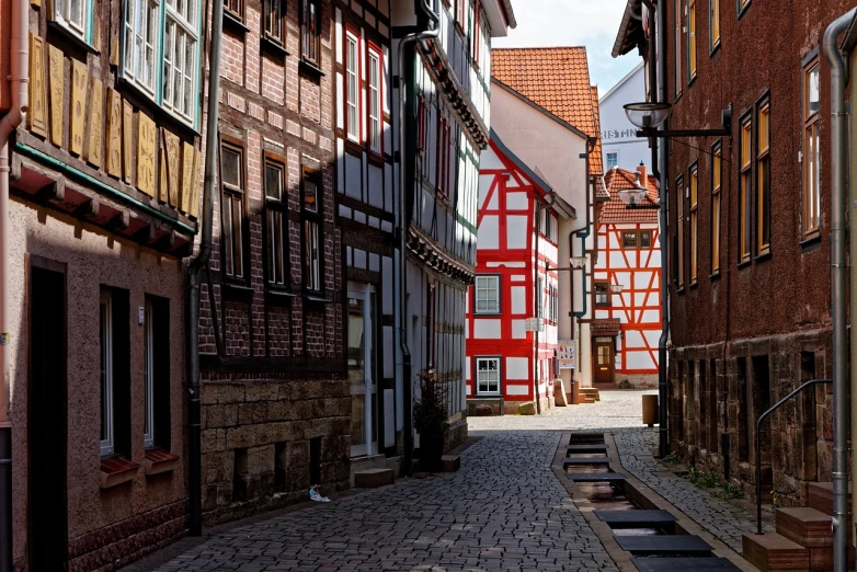 a narrow cobblestone street lined with old buildings, a photo, by Juergen von Huendeberg, shutterstock, timbered house with bricks, red and white colors, high quality image”