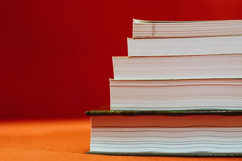 a stack of books sitting on top of a table, a stock photo, by Yi Jaegwan, simple red background, white and orange, shot from a low angle, meticulous detail