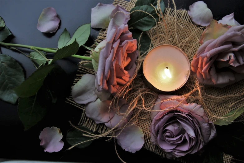 a close up of a candle surrounded by flowers, by Rhea Carmi, pexels, romanticism, black and purple rose petals, dark and beige atmosphere, pastel roses, remembrance